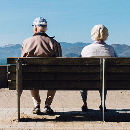 Elderly couple sitting on a bench looking out to sea and coast