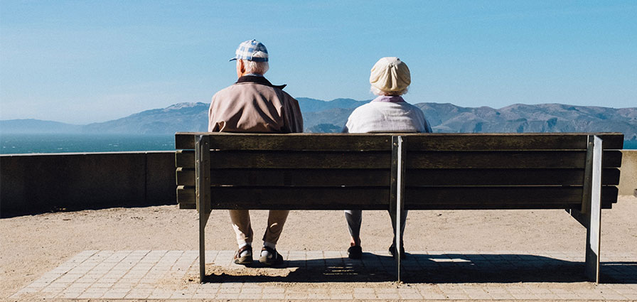 Elderly couple sitting on a bench looking out to sea and coast
