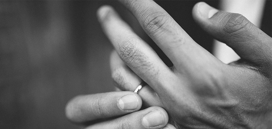 Black and white image of a hand holding thier wedding ring on their finger