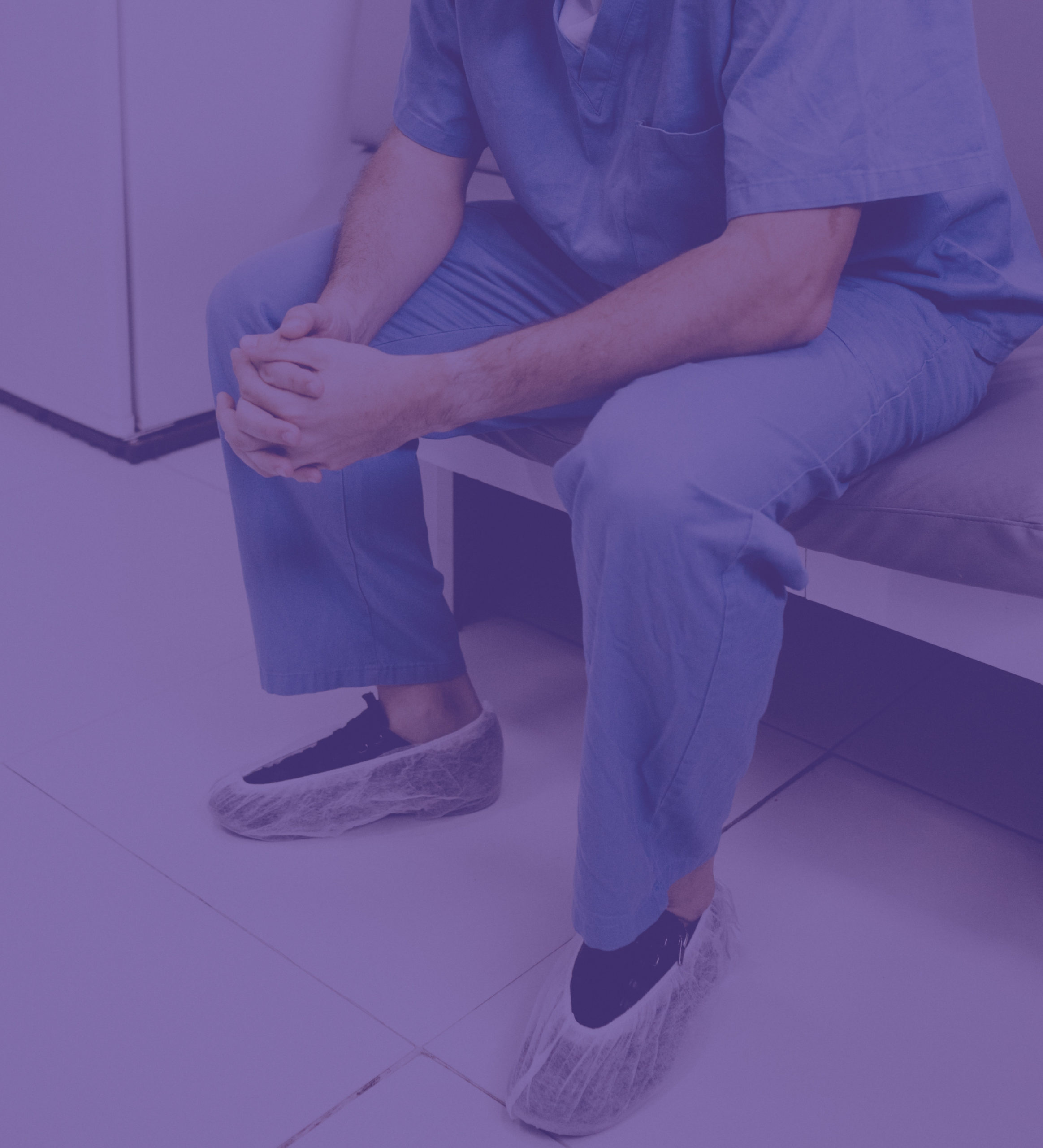 Nurse in blue scrubs clasping hands and sitting down