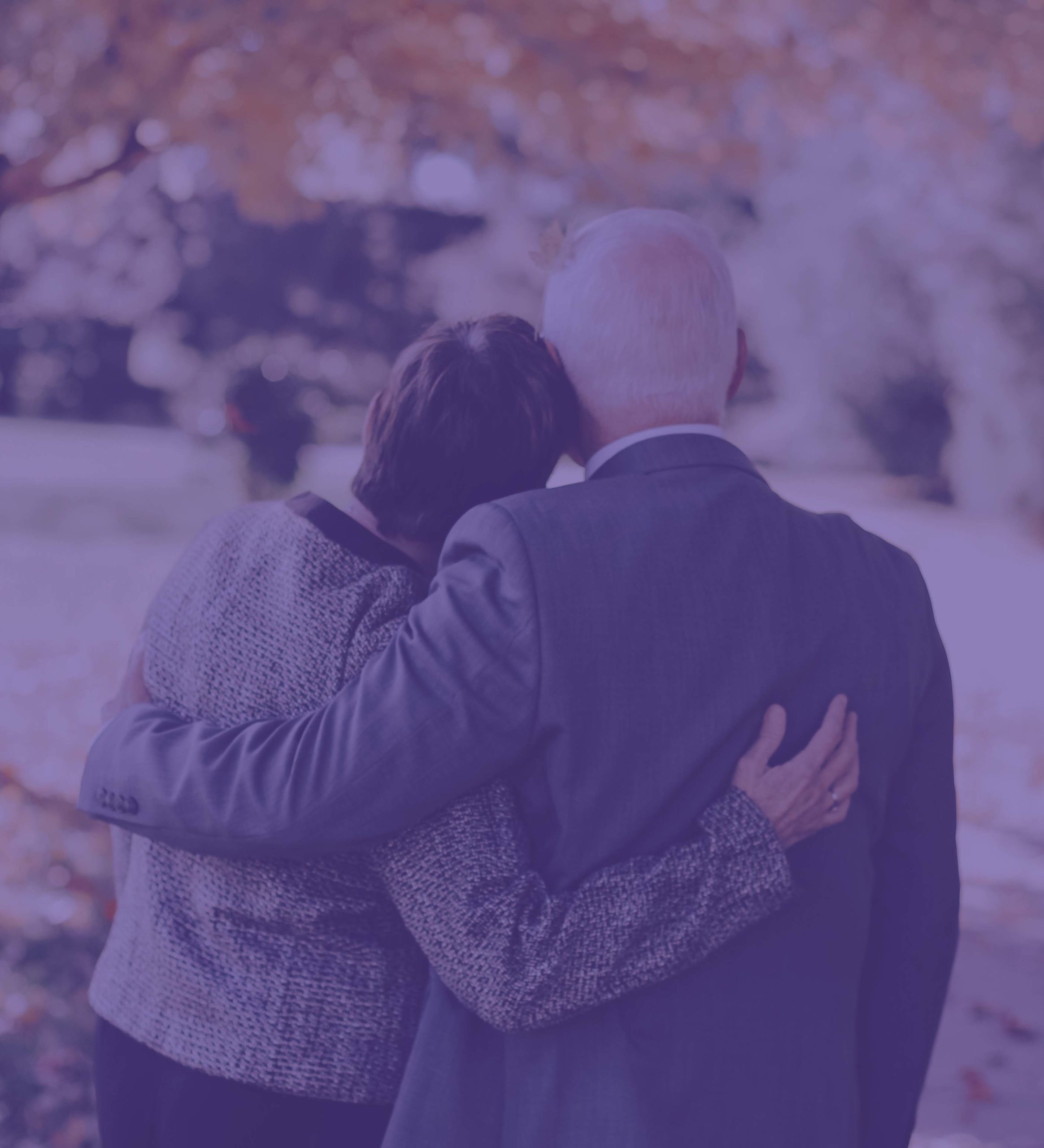 Woman with head on shoulder and arm around a man with white hair