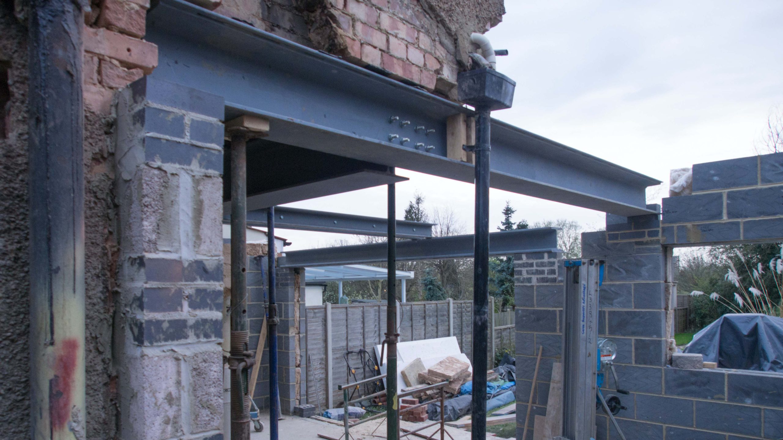 Scaffolding and metal beam holding up a half finished extension to a suburban house