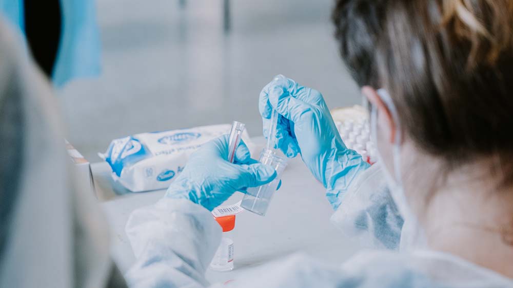 Looking over the shoulder of a nurse in protective scrubs while she prepares a testing kit