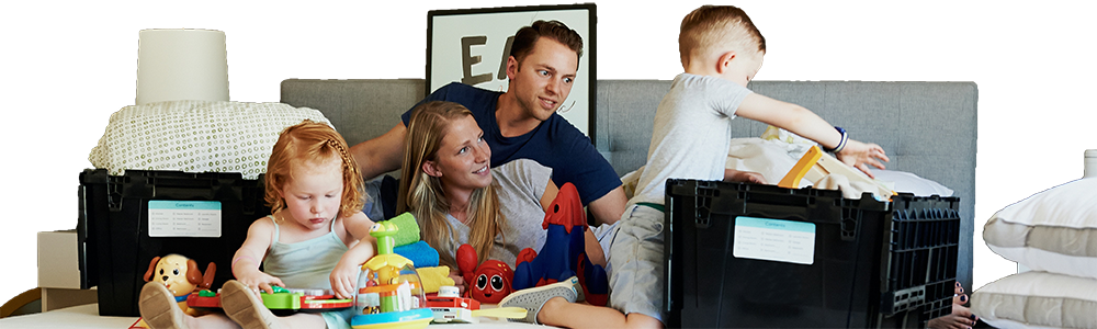 Young family sitting on double bed unpacking their moving home boxes