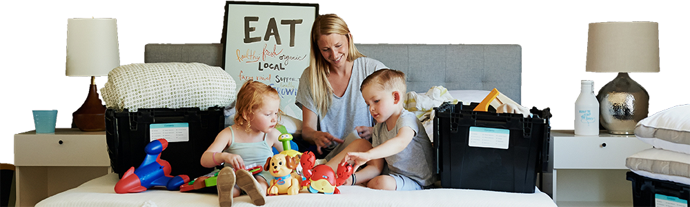 Young mother sitting on double bed with son and daughter surrounded by moving home boxes