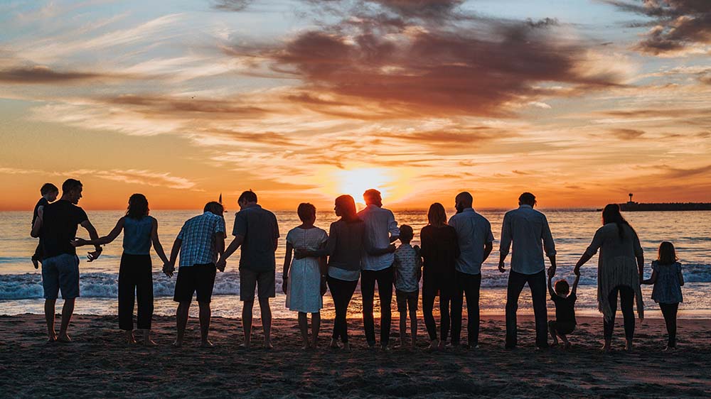 A big family on the beach silhouetted against the setting sun