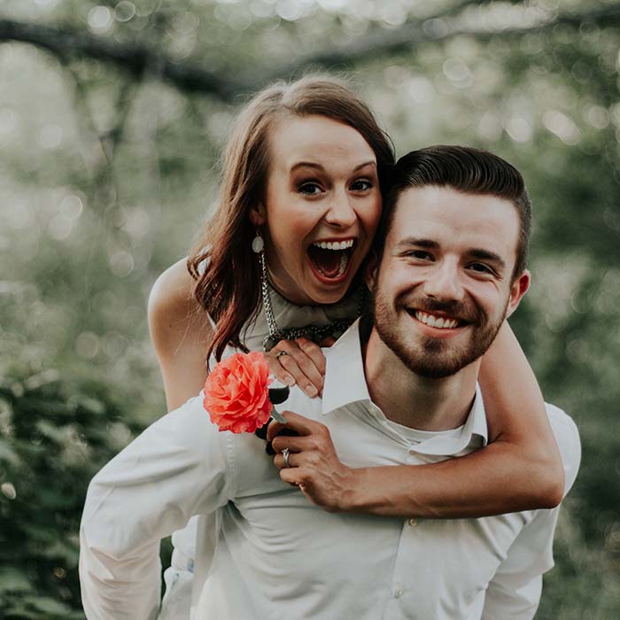 A young man giving a young lady a piggy-back and both are smiling