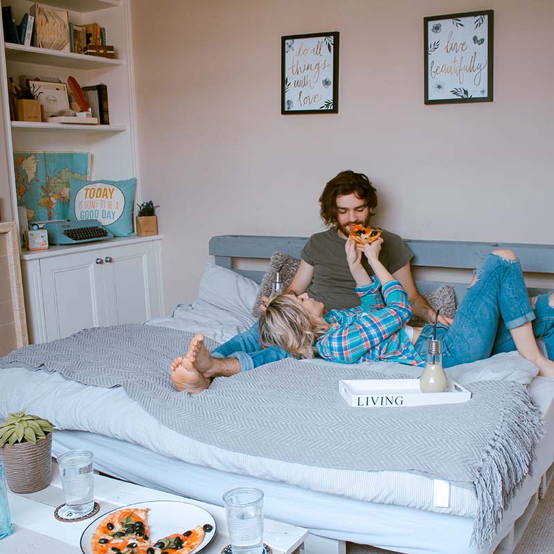 Couple lying on their bed eating pizza