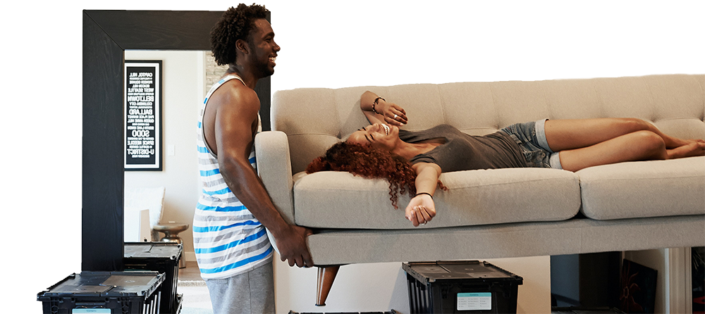 Man lifting a sofa into their new home with a woman lying on it