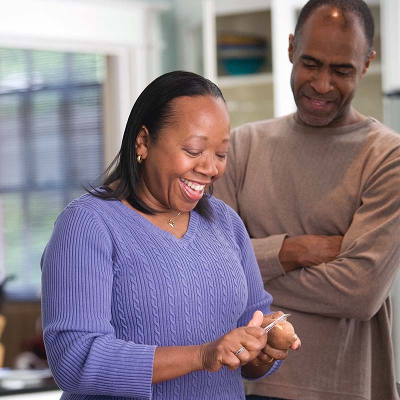 A smiling couple in the kitchen peeling potatoes