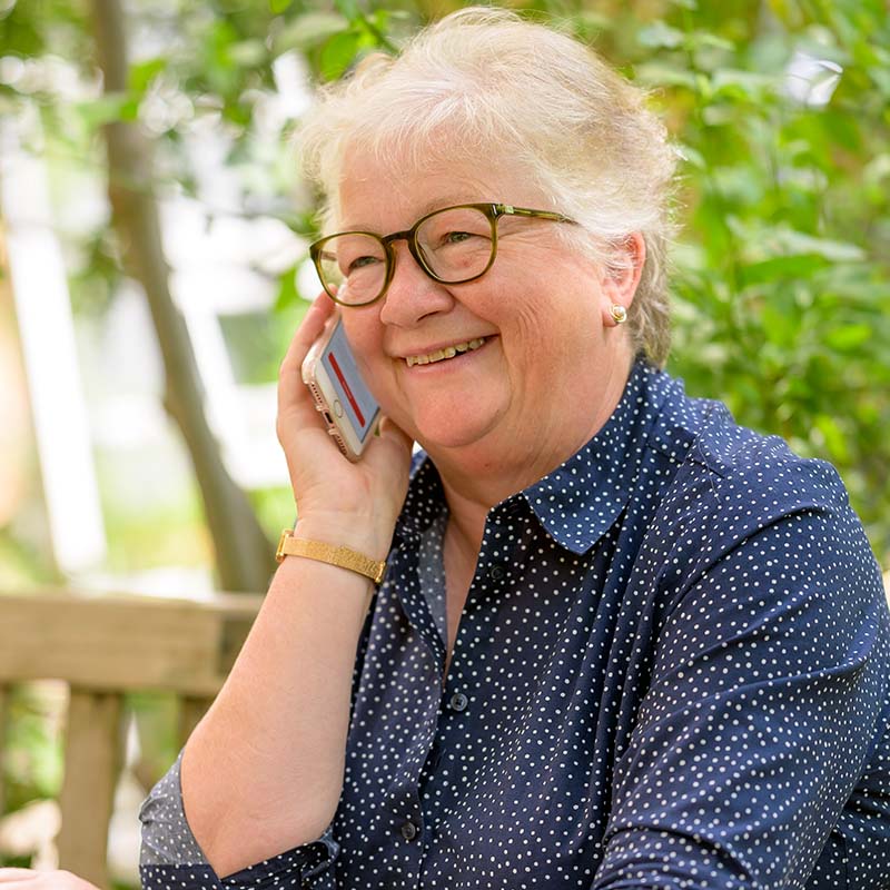 A mature lady with round glasses on her mobile phone in the garden