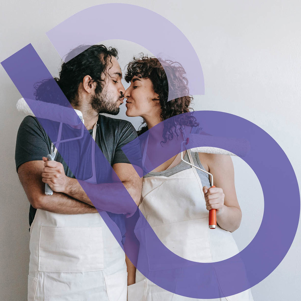 A woman and man holding paint rollers in white overalls and kissing.